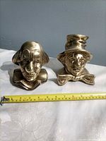 Front view of both brass clown bookends beside tape measure showing height