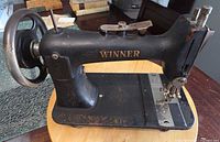 Left side profile of Winner sewing machine showing logo, base and wheel