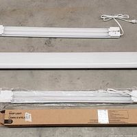 Two loose LED shop light fixtures and one boxed unit laid out