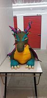 Front view of large ride-on plush dragon on table