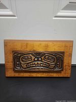 Front view of rectangular wood plaque showing carved face motif
