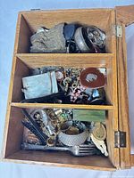 Overview of open wooden box showing mixed jewelry, watches, metalware items