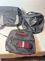 Three bags laid out: NuWave tote, grey-black backpack, black-red backpack