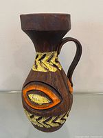 Front view of brown ceramic pitcher vase with yellow and orange relief pattern