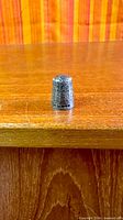 View of entire thimble standing upright on wood surface displaying overall shape and decoration