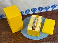 Bangle seated in original yellow presentation box with lid beside