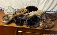 Nine vintage fur hats and collars displayed on wooden surface