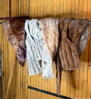 Four mink fur stoles draped over railing showing color range and linings