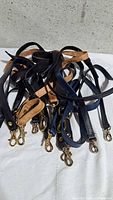 Pile of seven assorted leather bag straps with metal hooks displayed on white surface