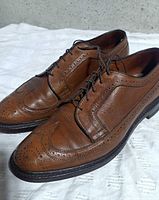 Left side view of both shoes showing brown leather, brogue details, overall condition