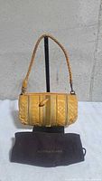 Front view of yellow Intrecciato shoulder bag on stand with dust bag beneath