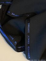 Edge of fabric showing blue selvedge text '100% WORSTED FANCY SUITING' confirming material
