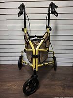 Front view showing yellow frame, three wheels, plaid bag, handle brakes