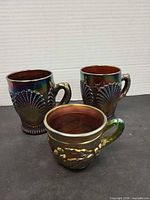 Front view of all three iridescent carnival glass mugs showing patterns and handles
