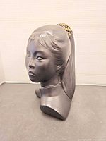 Front-side view of black composite female bust showing facial features and ponytail