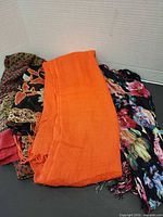 Three scarves: orange solid, black multicolour floral streak, red/gold patterned partially visible
