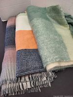 Three scarves folded: fuzz green plaid, color-block, plaid/gradient