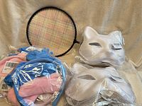 Group shot of badminton racket, two bags of blank masks, plush headpiece