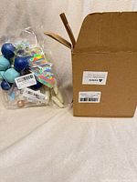 Sealed bag containing foam ball cake toppers beside plain cardboard box
