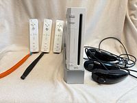 Console on stand, three Wii Remotes, three Nunchuks and cabling visible