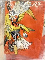 Front of packaged headscarf showing orange fabric with floral and butterfly print