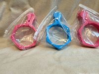 Three plastic sublimation clamps sealed in bags, two pink and one blue