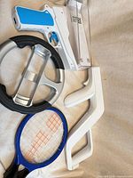 Overview showing steering wheel, blue-handled gun holder, white zapper part, blue tennis racket