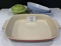 Top view of four ceramic baking dishes: red rectangular pan foreground, apple green lidded casserole, two nested light blue oval dishes