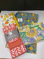 Group shot of all kitchen linens: packaged tablecloth, apron, dish mat set, fruit tea towels