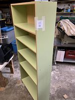 Side view of mint green bookcase showing five installed shelves and loose shelf on top