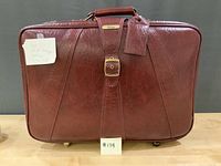 Front view of large burgundy Jetliner suitcase showing textured vinyl, buckle strap detail and luggage tag