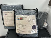Front view of two packaged INVER sofa slipcovers showing labels and grey colour