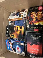 Box with multiple VHS tapes including Remember the Titans, October Sky, The Horse Whisperer