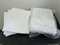 Stack of unfolded white pillowcases beside sealed stack on black surface