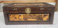 Front view of carved wooden chest showing scenic panel and brass latch