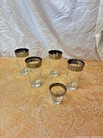 Five glasses on fabric surface showing silver rims