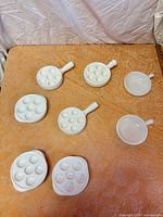 Eight white porcelain pieces grouped on table – six plates show six wells each, two ramekins have smooth interiors