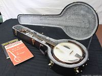 Banjo inside open hard case with strap and instructional booklets