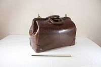 Front three-quarter view of brown leather doctor’s bag with ruler for scale