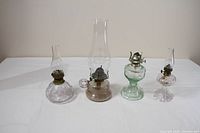 Group shot of four glass oil lamps showing sizes, colours and chimneys