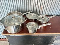 Full view of five stainless pots and pans with glass lids on tabletop
