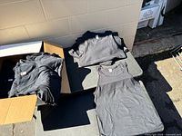 Open box and stacks of black tank tops on table