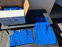 Open box showing stacked royal blue tank tops and two samples laid out