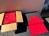 Open box containing stacked red tank tops with one laid out