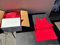 Open box showing stacked red tank tops and one laid out