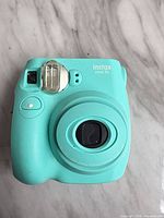 Front view of Fujifilm Instax Mini 7S camera showing lens, flash, and mint color