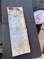 Boxed starburst wall decor showing gold-tone spokes and clear acrylic ball tips