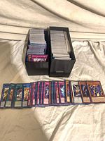 Two black long card boxes filled with unsleeved Yu-Gi-Oh! cards, row of assorted cards displayed