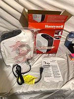 Heater wrapped in plastic, power cord, box, manual visible