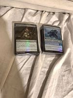 Two sealed stacks of sleeved foil MTG cards on fabric background